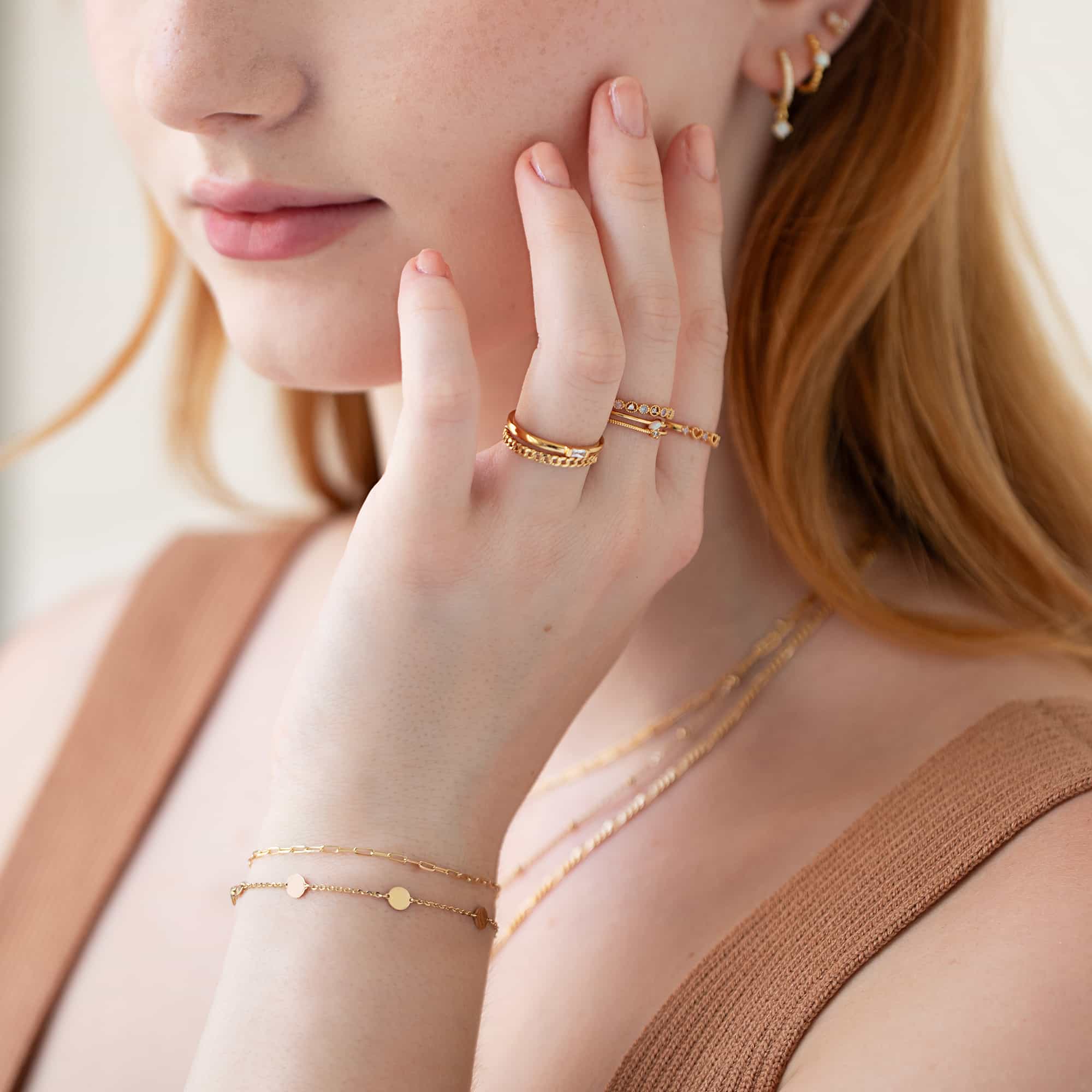 Gold stacking rings and layered disc bracelets shown on a model's hand