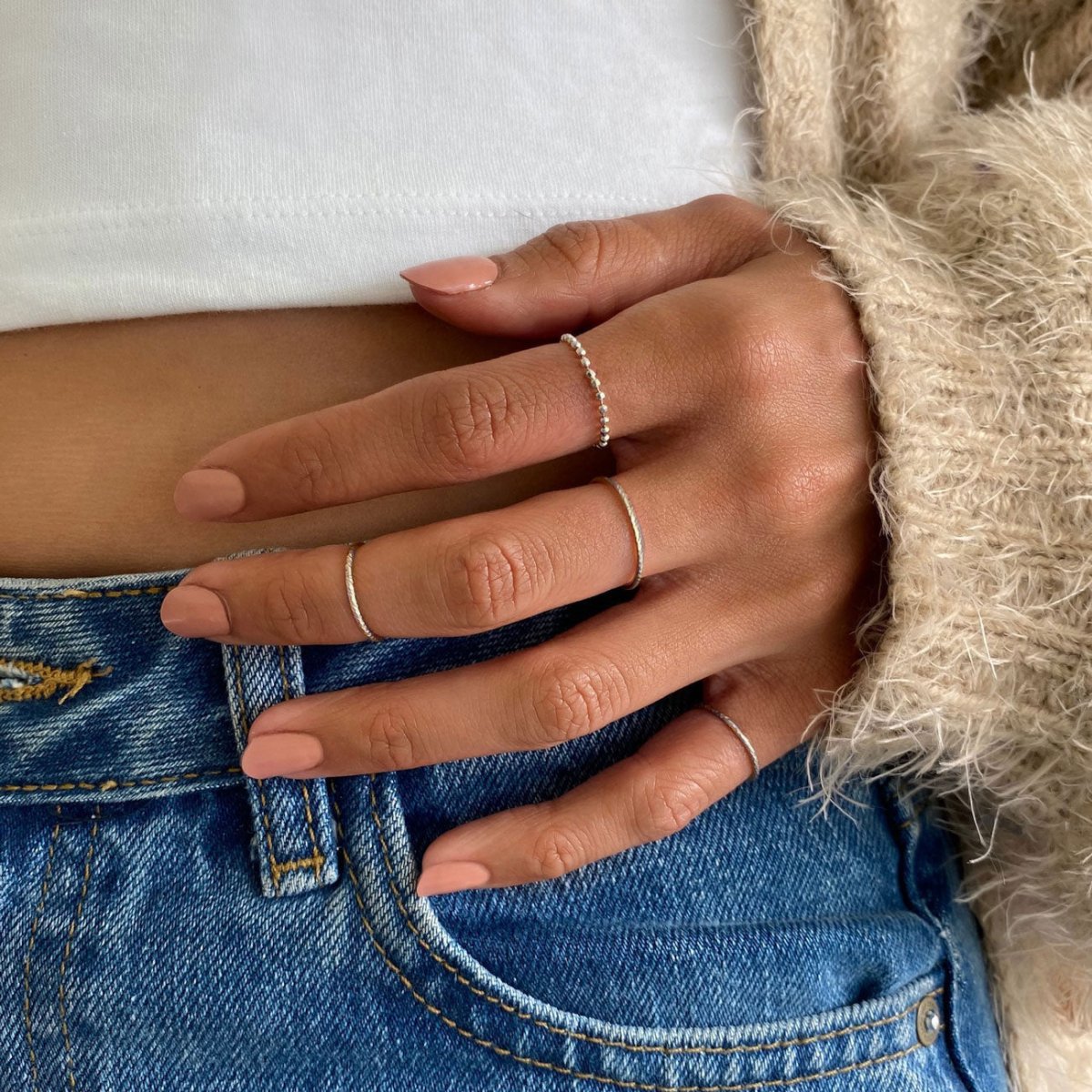 Sterling silver thin beaded stacking rings worn across the fingers, shown on a model's hand