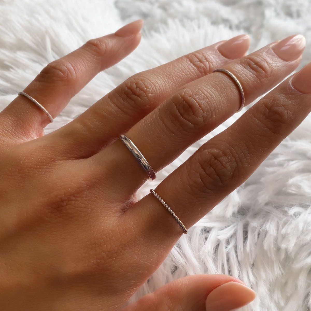 Sterling silver thin twisted rope ring worn in a stack, shown on a model's hand on white fur