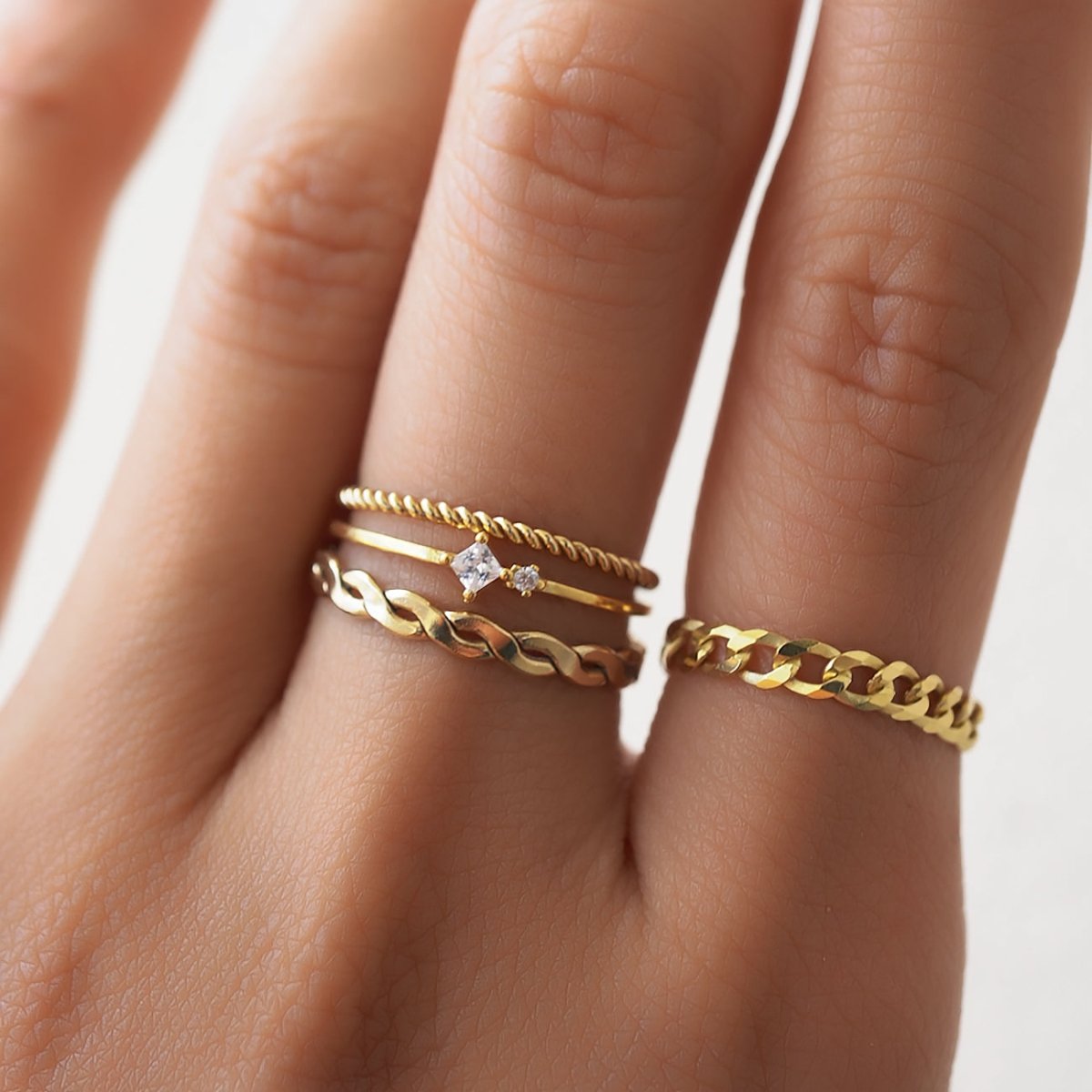 Gold-filled woven braided ring shown on a model's finger in a stack with thin and curb-chain rings