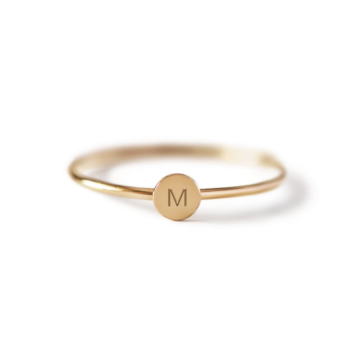 Gold-filled thin band ring with a small round disc engraved with an initial, on a white background