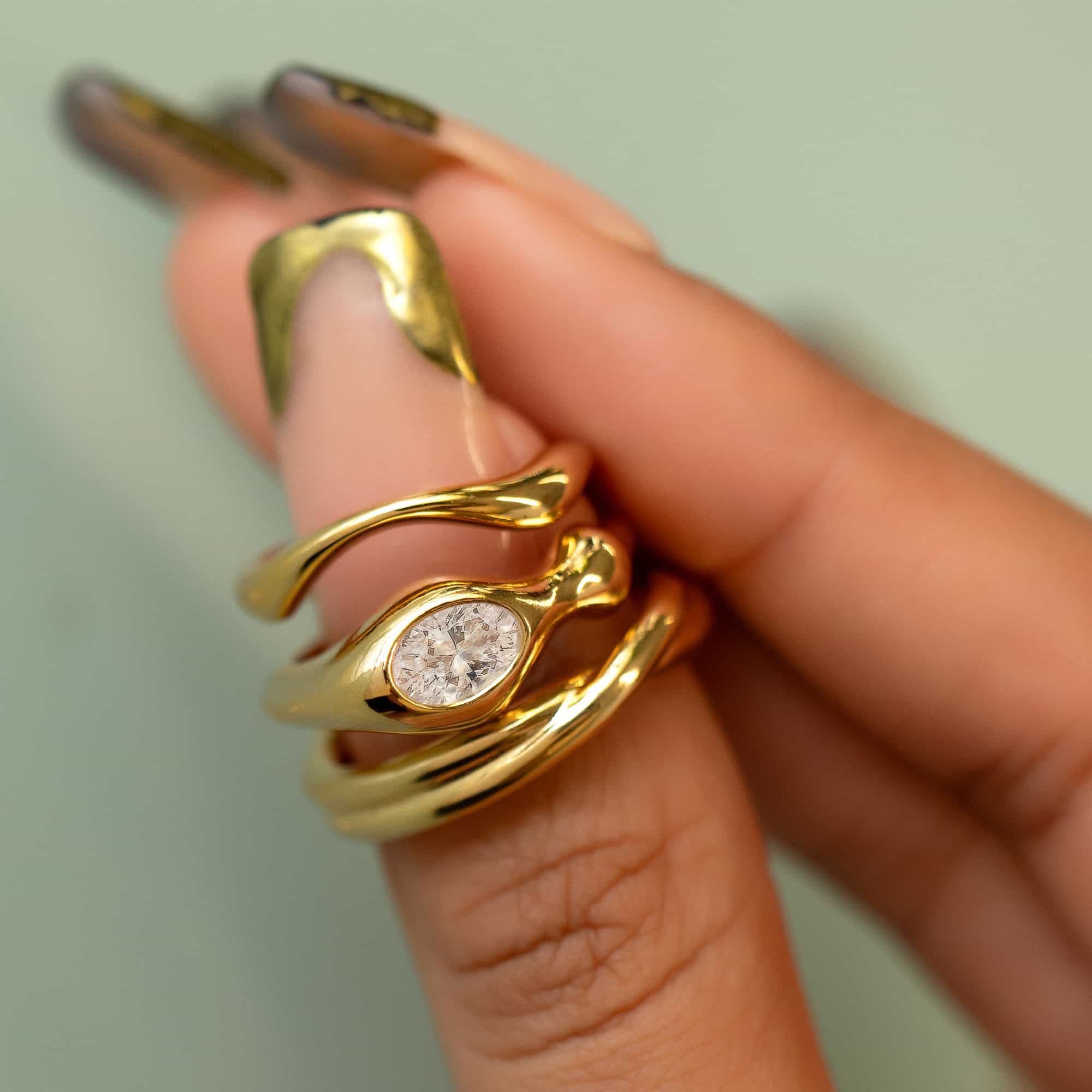 Gold vermeil sculptural ring with an oval white zirconia, held between fingers in close-up detail