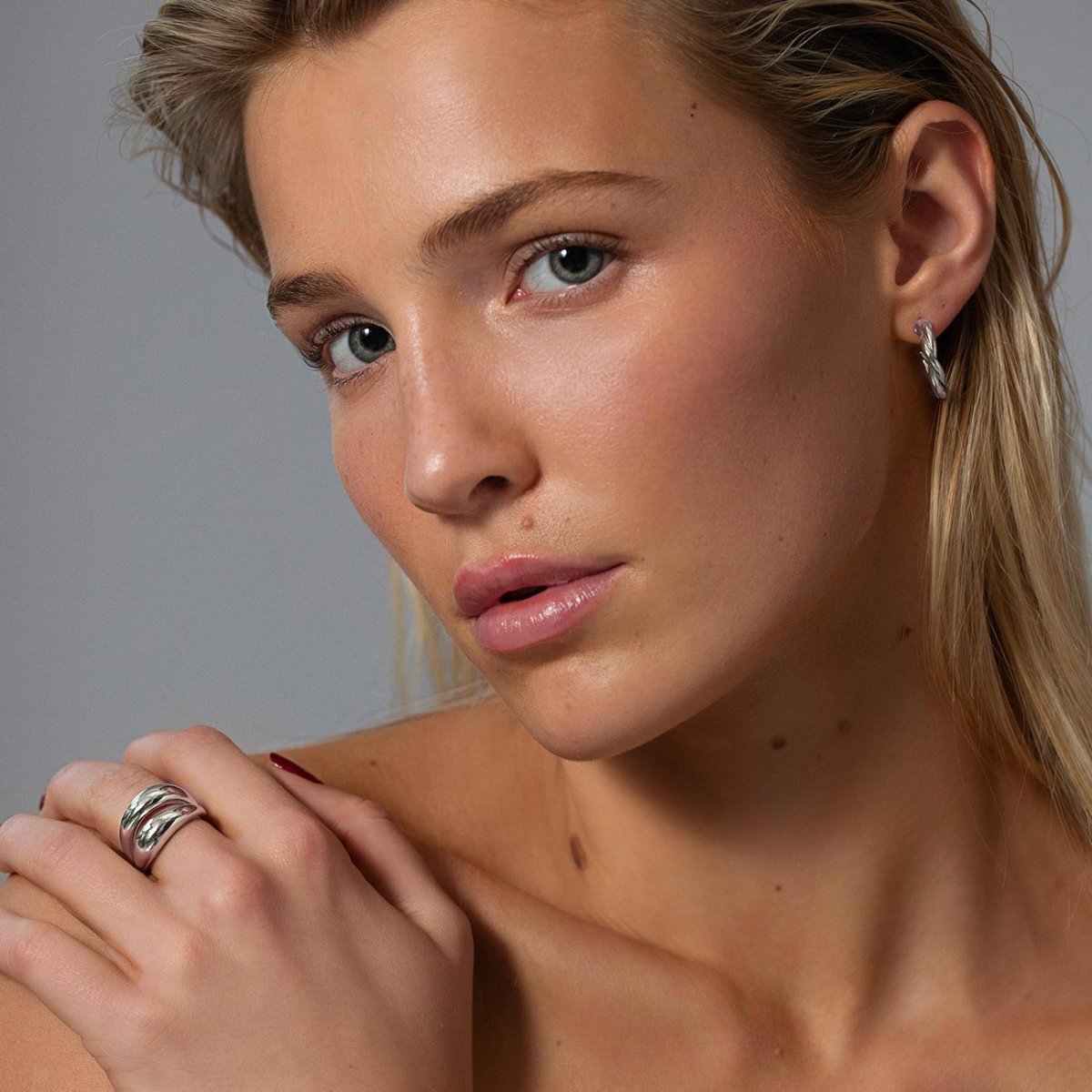 Sterling silver twisted rope C-hoop earring shown on a model's lobe with a twisted ring on her hand