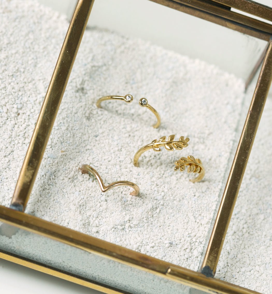 Gold vermeil open ring with clear stones, styled with leaf and chevron rings on white sand