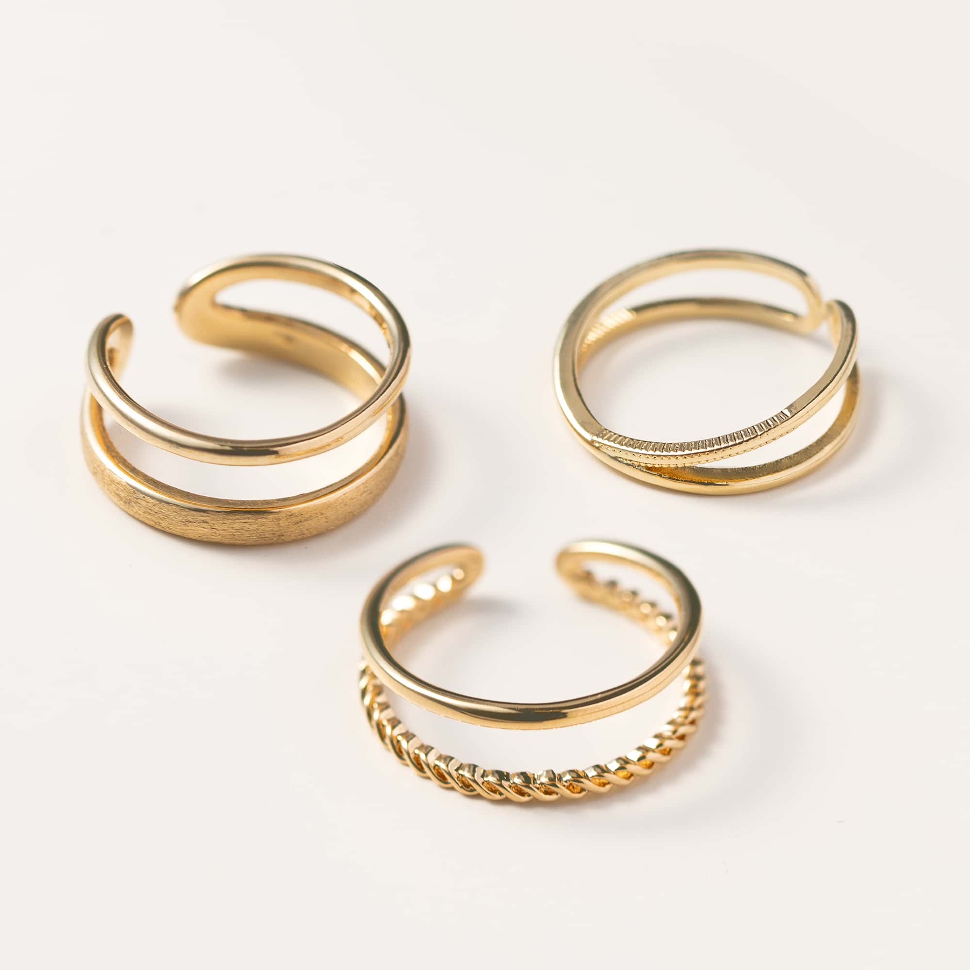 Three gold open stacking rings with plain, beaded and rope-twist bands, on a white background