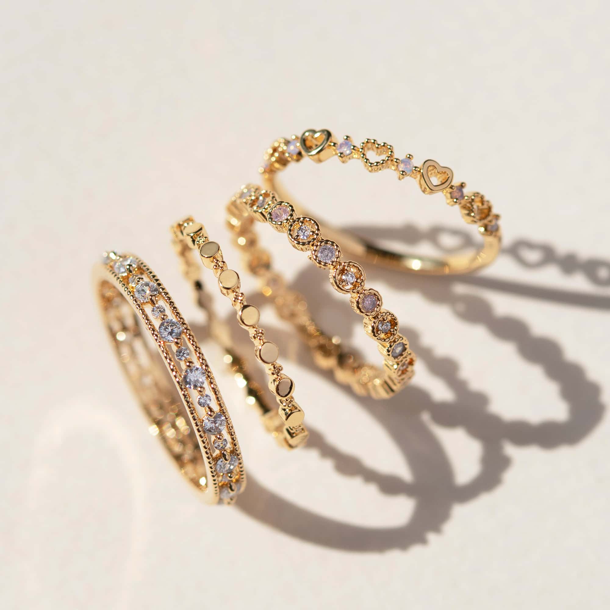 Four gold stacking rings with clear stones and beaded bands, on a cream background