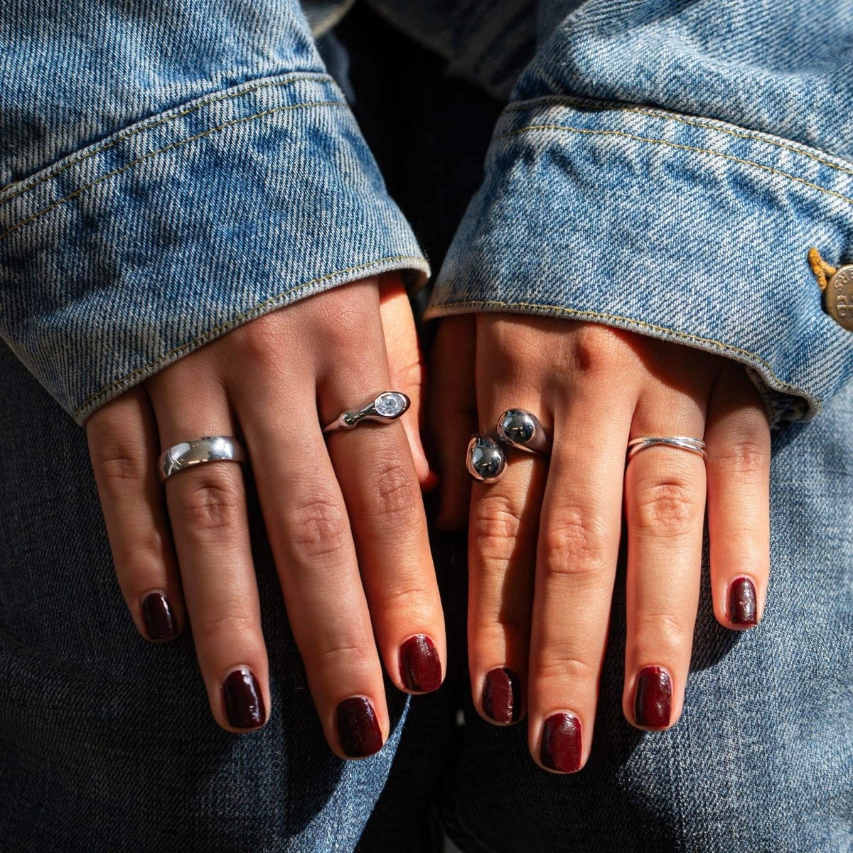 Sterling silver X stacker ring with a crossover band, shown on a model's finger with denim sleeves