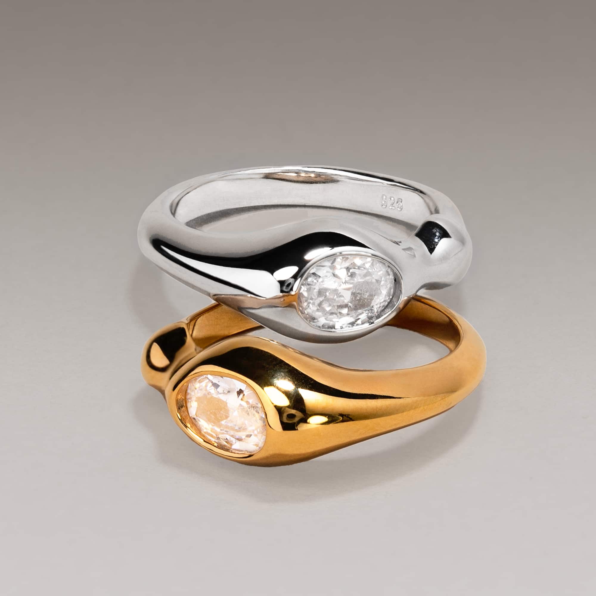 Sterling silver and gold sculptural rings with oval white zirconia stones, on a gray background
