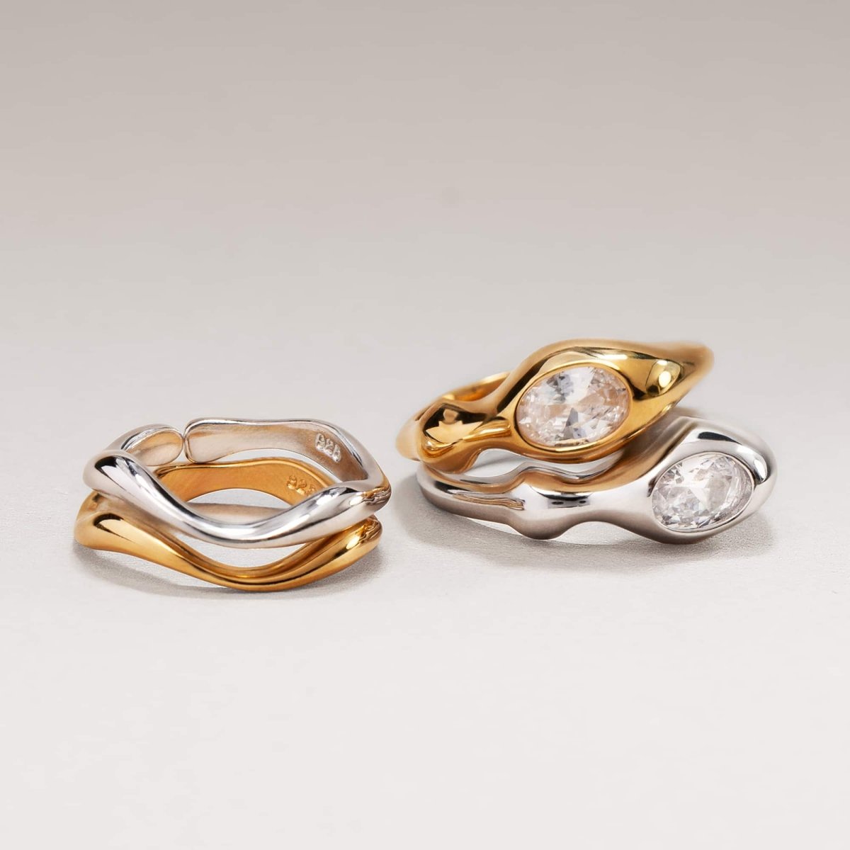 Gold vermeil and silver sculptural white zirconia rings with wavy bands, shown together on a cream background