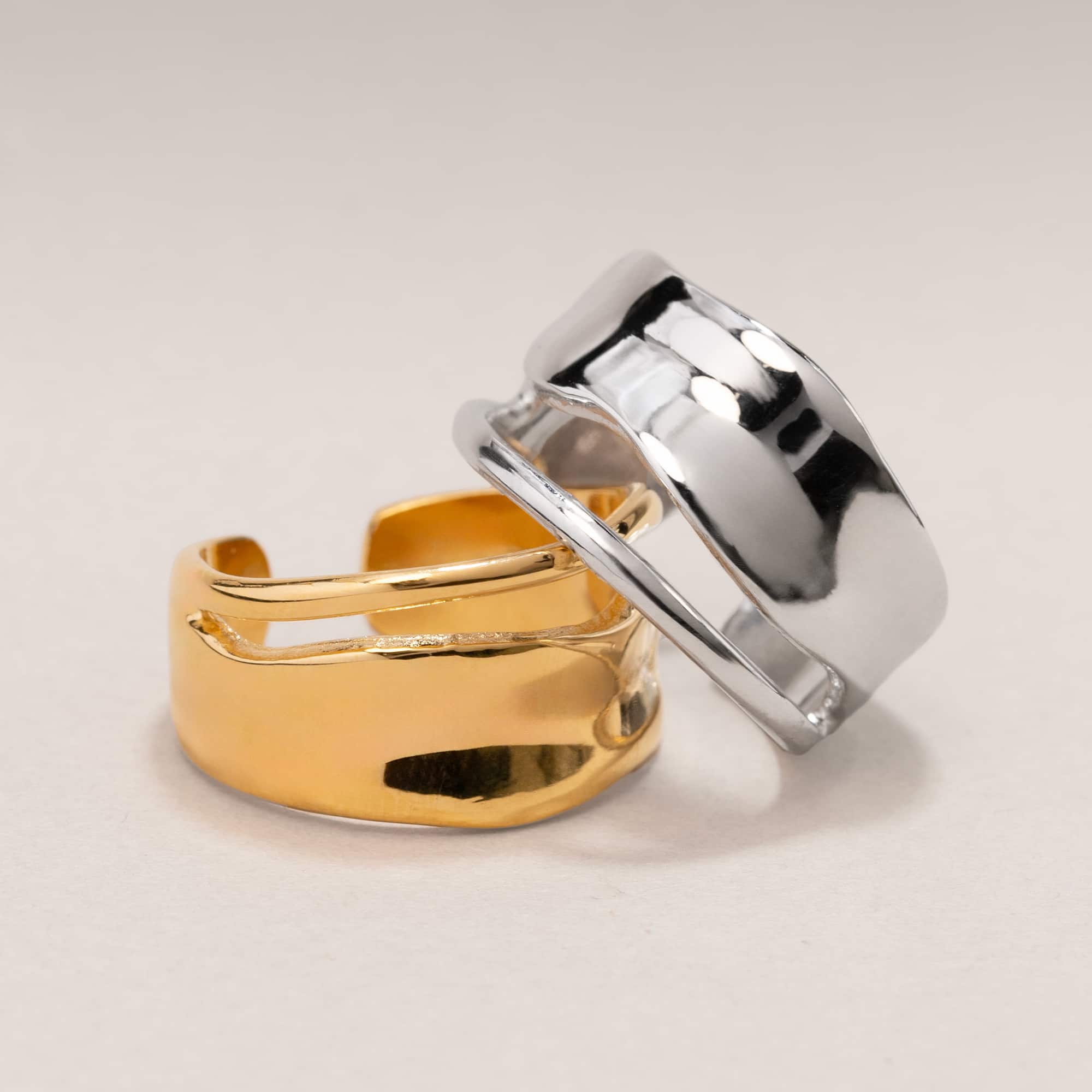 Sterling silver melted wide band statement ring beside a gold one, on a white background