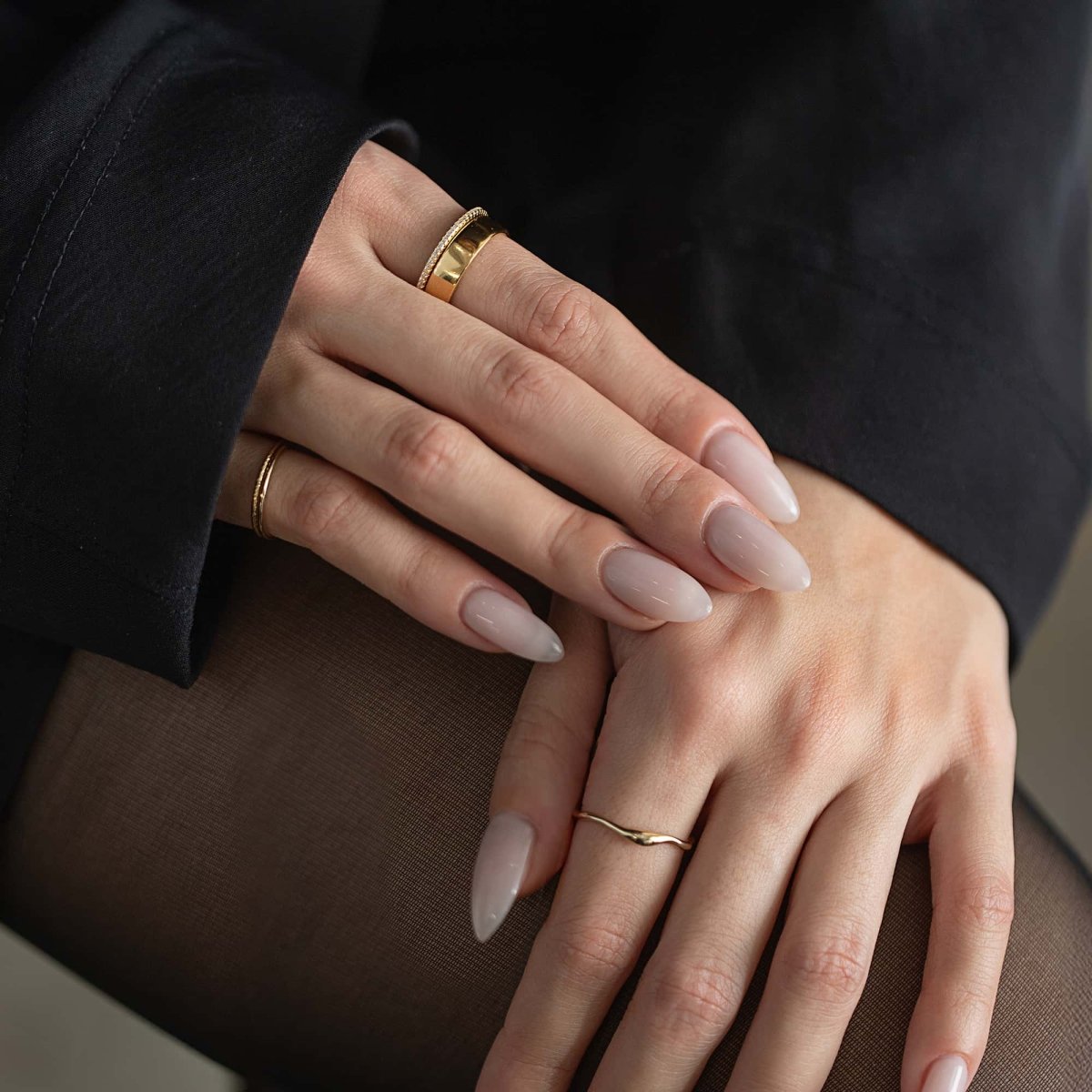 14K gold dainty wave stacking ring worn on a hand resting over a darker stacked band
