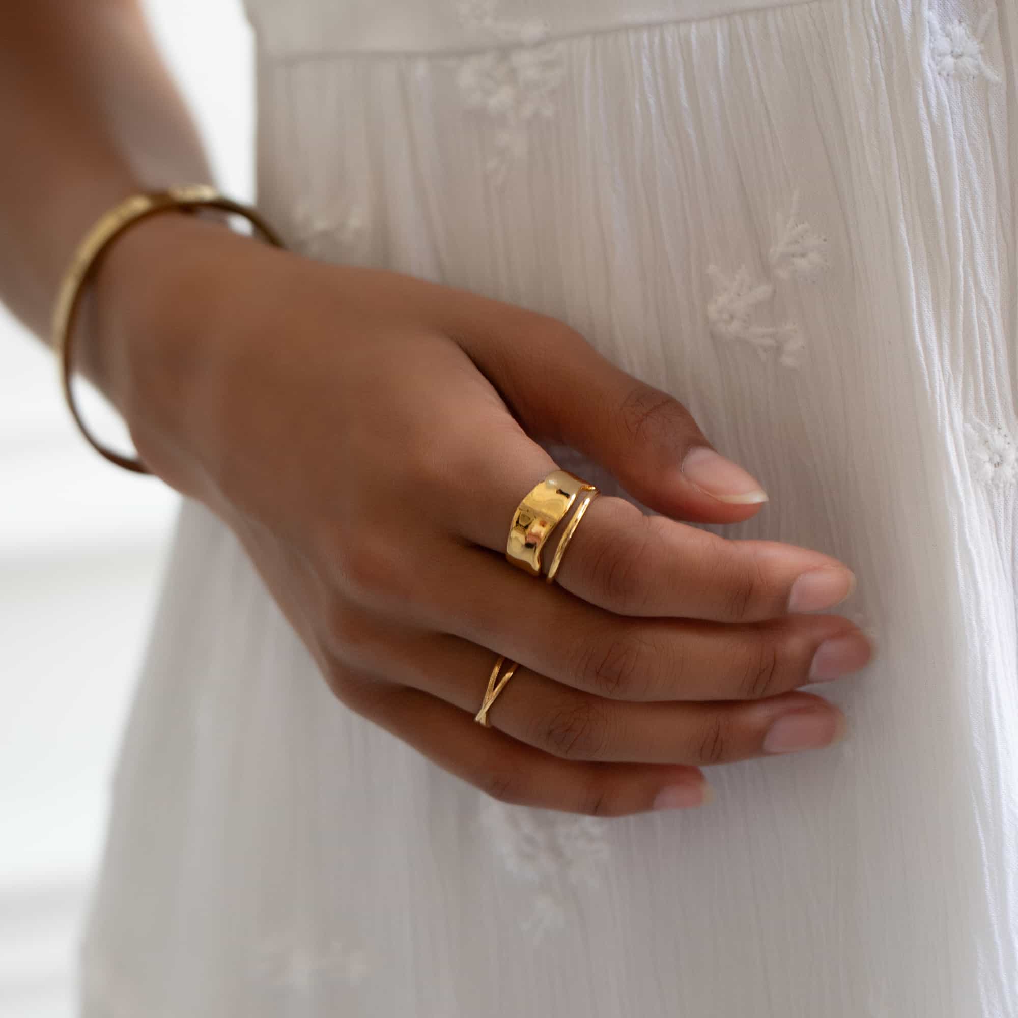 Gold wide hammered band ring and thin X ring shown stacked on a model's hand