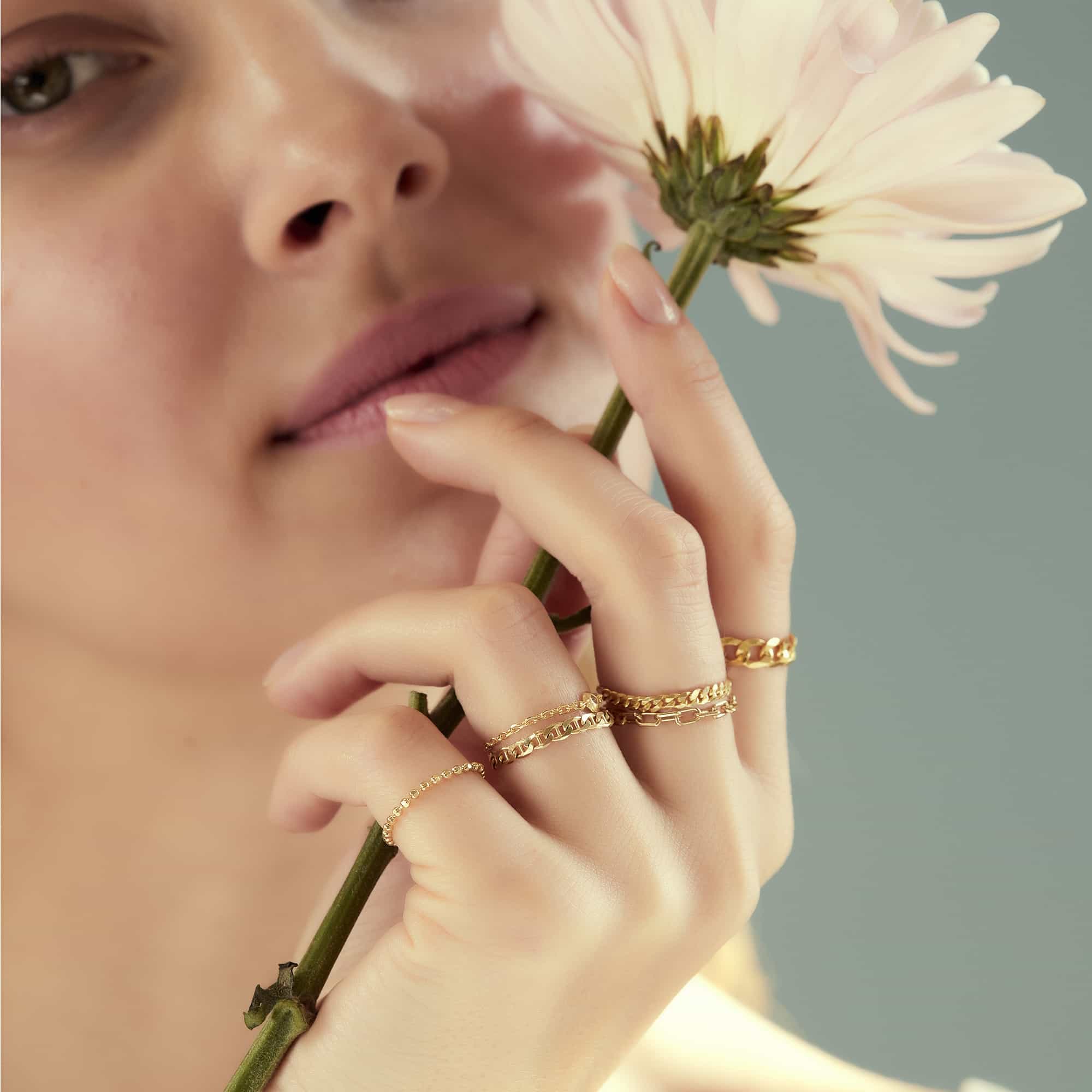 Three gold chain-link and beaded stacking rings worn together on a model's fingers