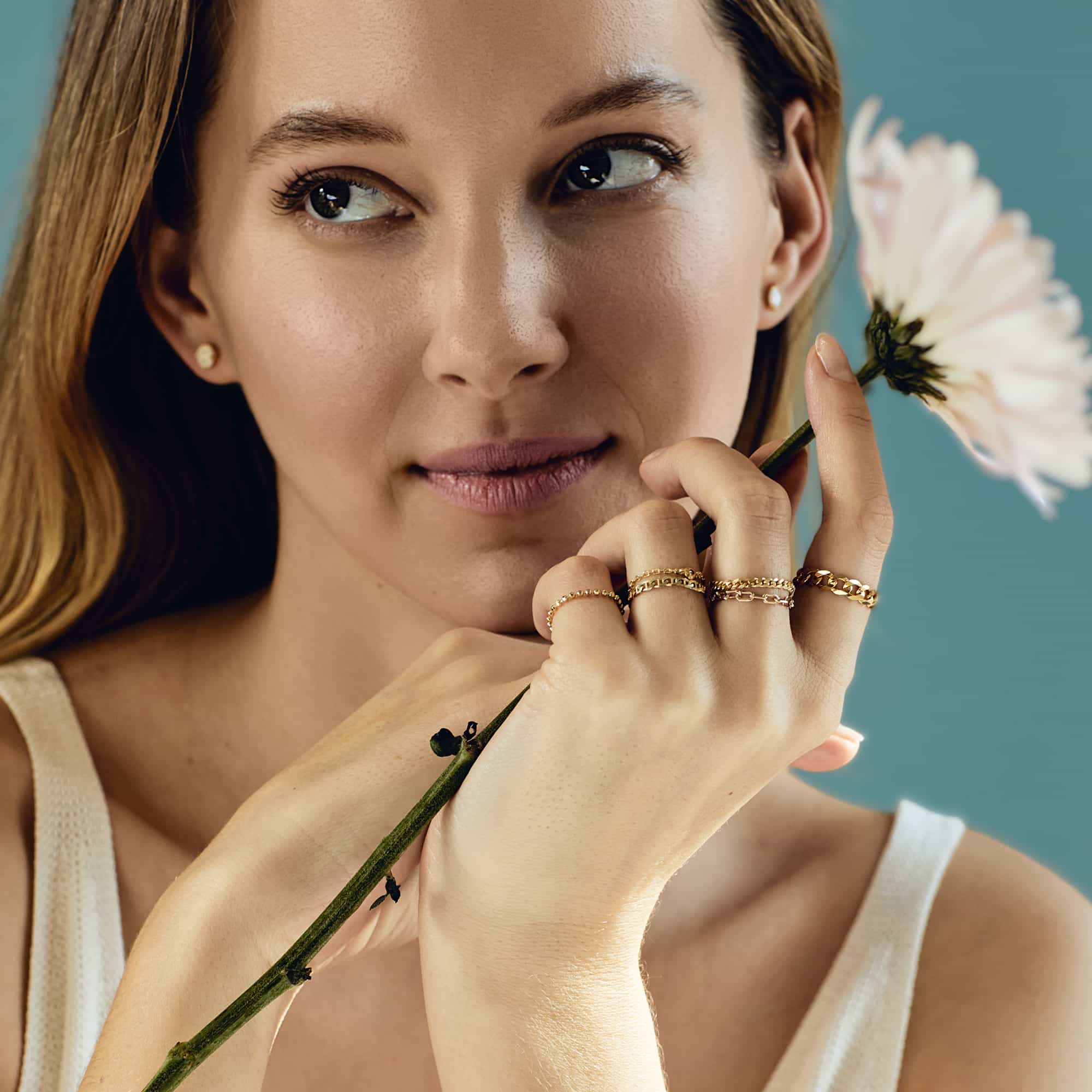 14K gold curb chain ring among stacked rings on a model's hand holding a flower