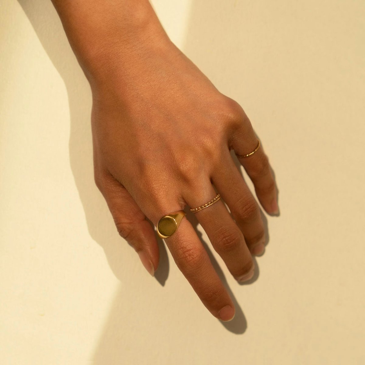 Gold vermeil round signet ring shown on a model's hand laid flat on a cream surface