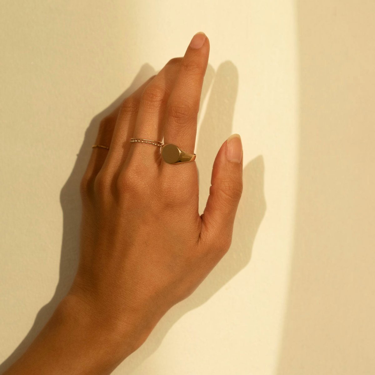 Gold vermeil round signet ring worn on a model's finger, shown against a warm cream wall
