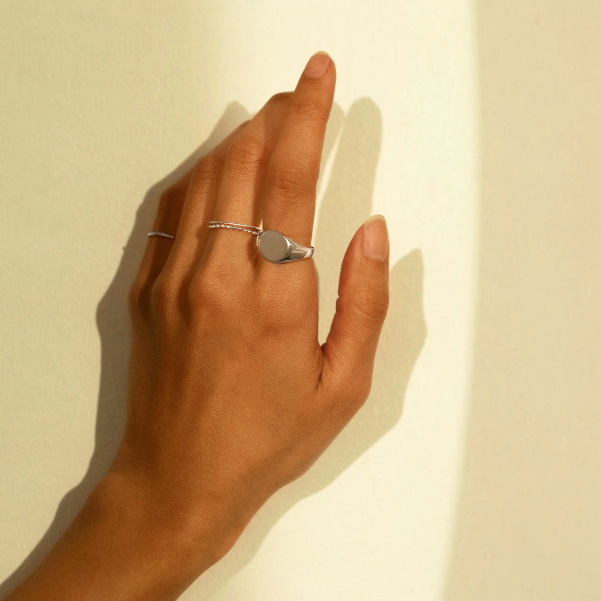 Sterling silver oval signet ring worn on a model's finger against a cream wall
