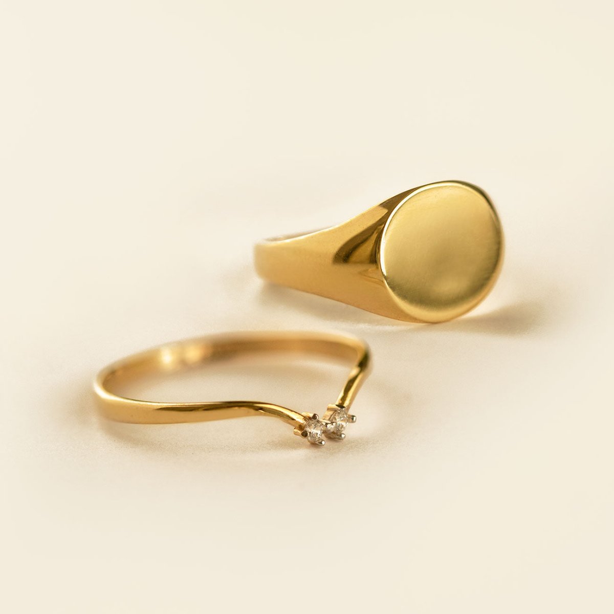 Gold vermeil oval signet ring with a plain face, shown beside a thin ring on a cream background