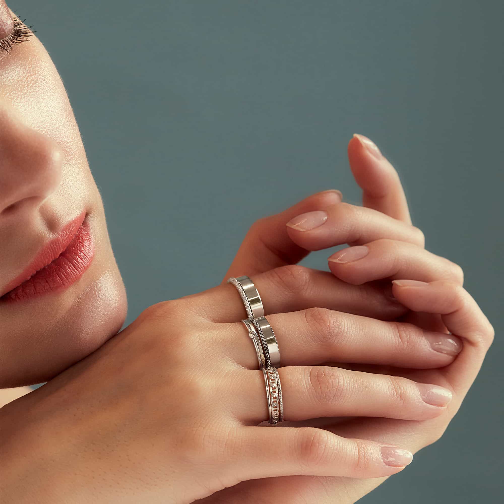 Sterling silver flat and rope band rings stacked on a model's hand near her face