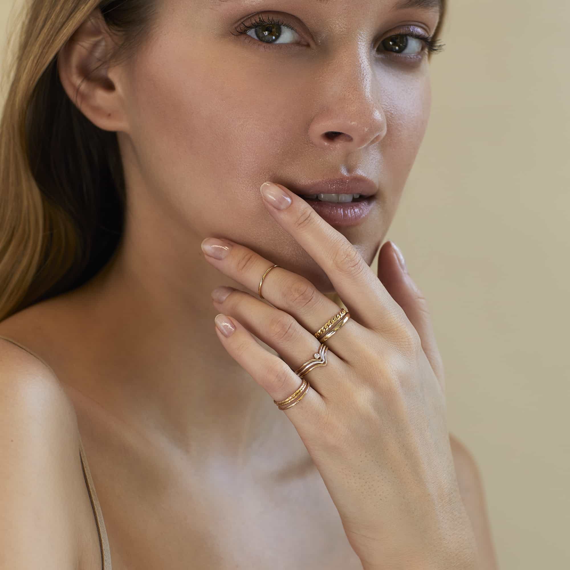 Stack of thin gold rings shown on a model's hand near the face