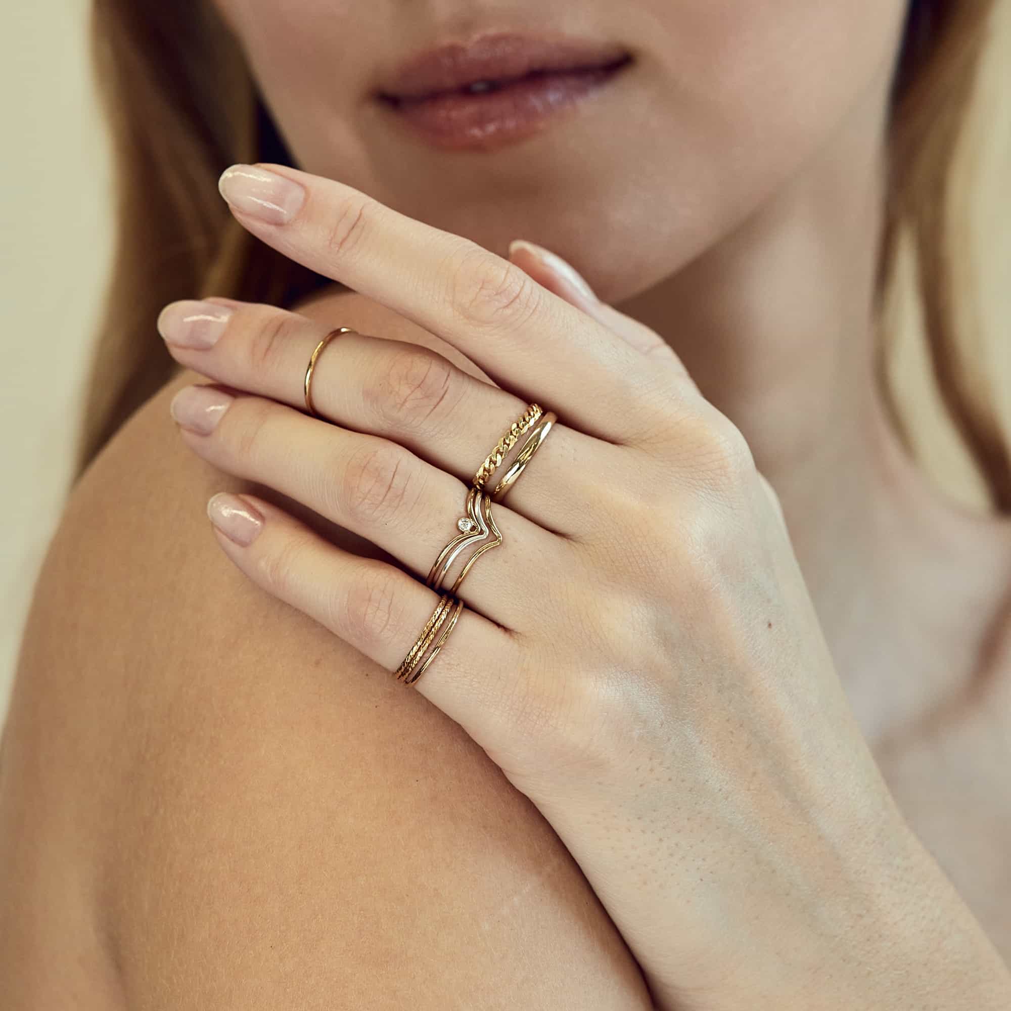 Gold thin, twisted and curb chain stacking rings worn on a model's hand at the shoulder