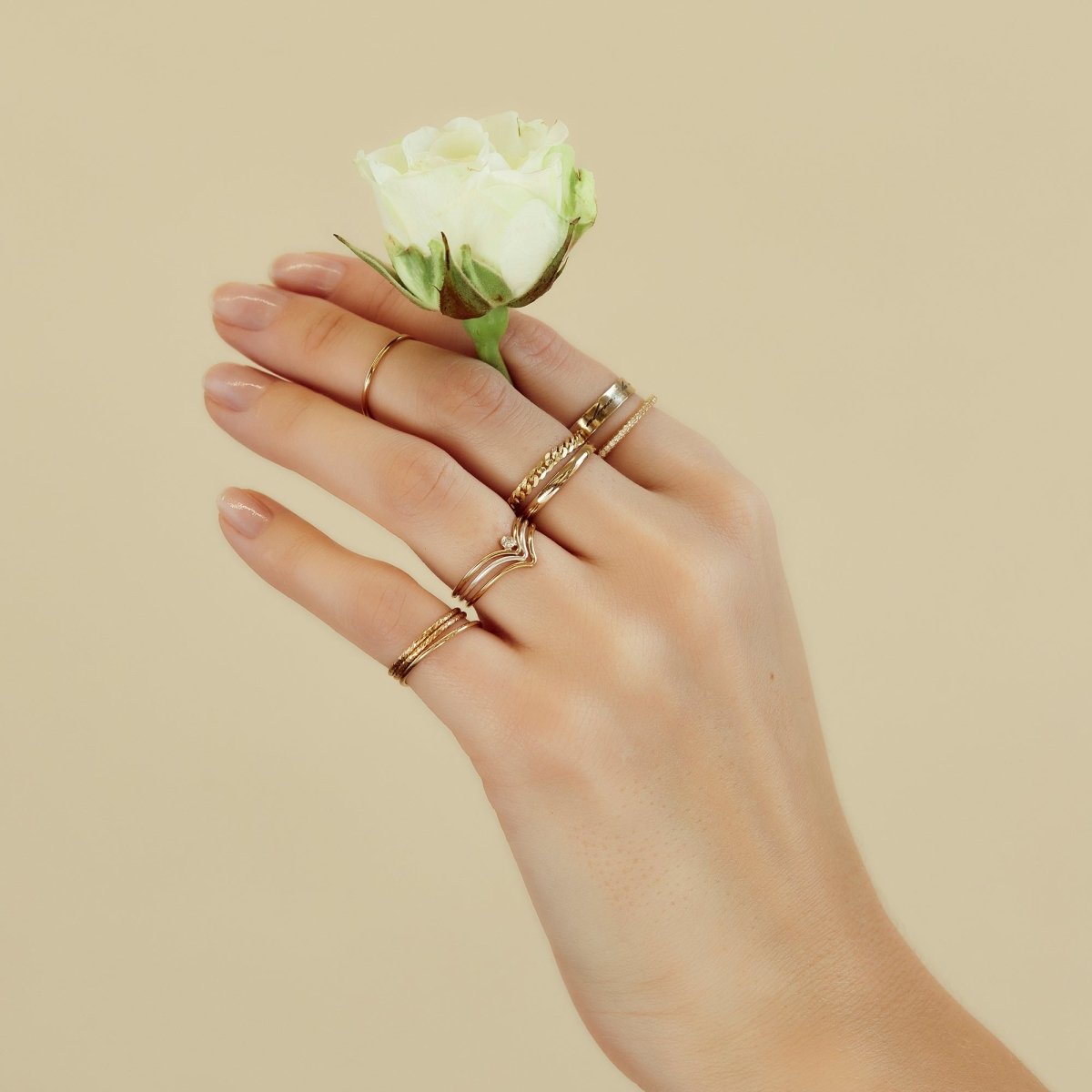 Gold-filled chevron ring stacked with other rings, shown on a model's hand holding a rose