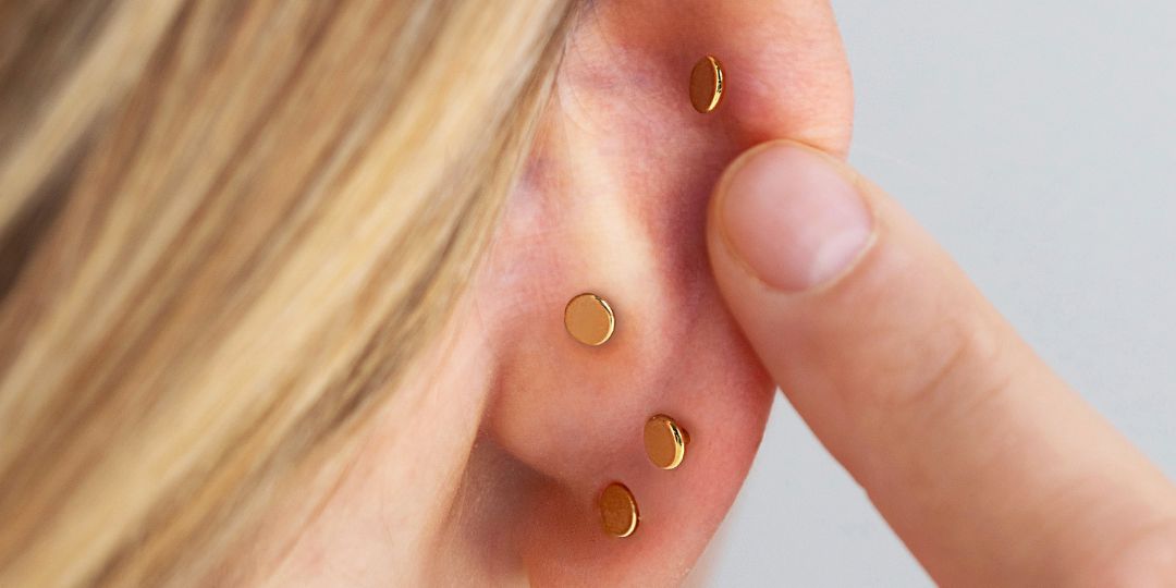 Close-up of an ear worn with four flat round gold discs across the lobe, helix and conch piercings