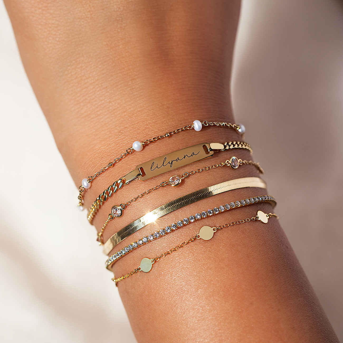 Multiple gold bracelets from AMYO in engraved, pearl, and crystal designs, perfect for stacking and thoughtful gifting.