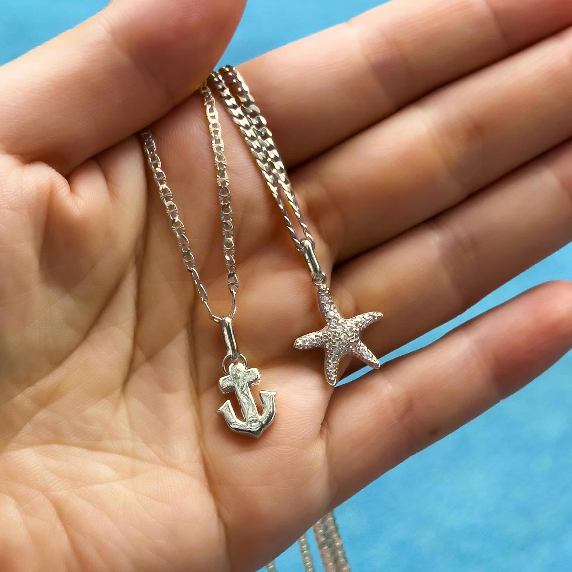 Silver anchor charm and a pavé starfish charm on chains, held in an open palm
