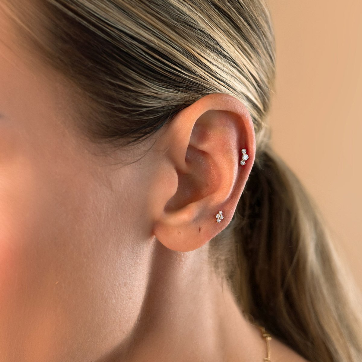 Gold Titanium flat back stud earrings shown in the helix and lobe on a model's ear.
