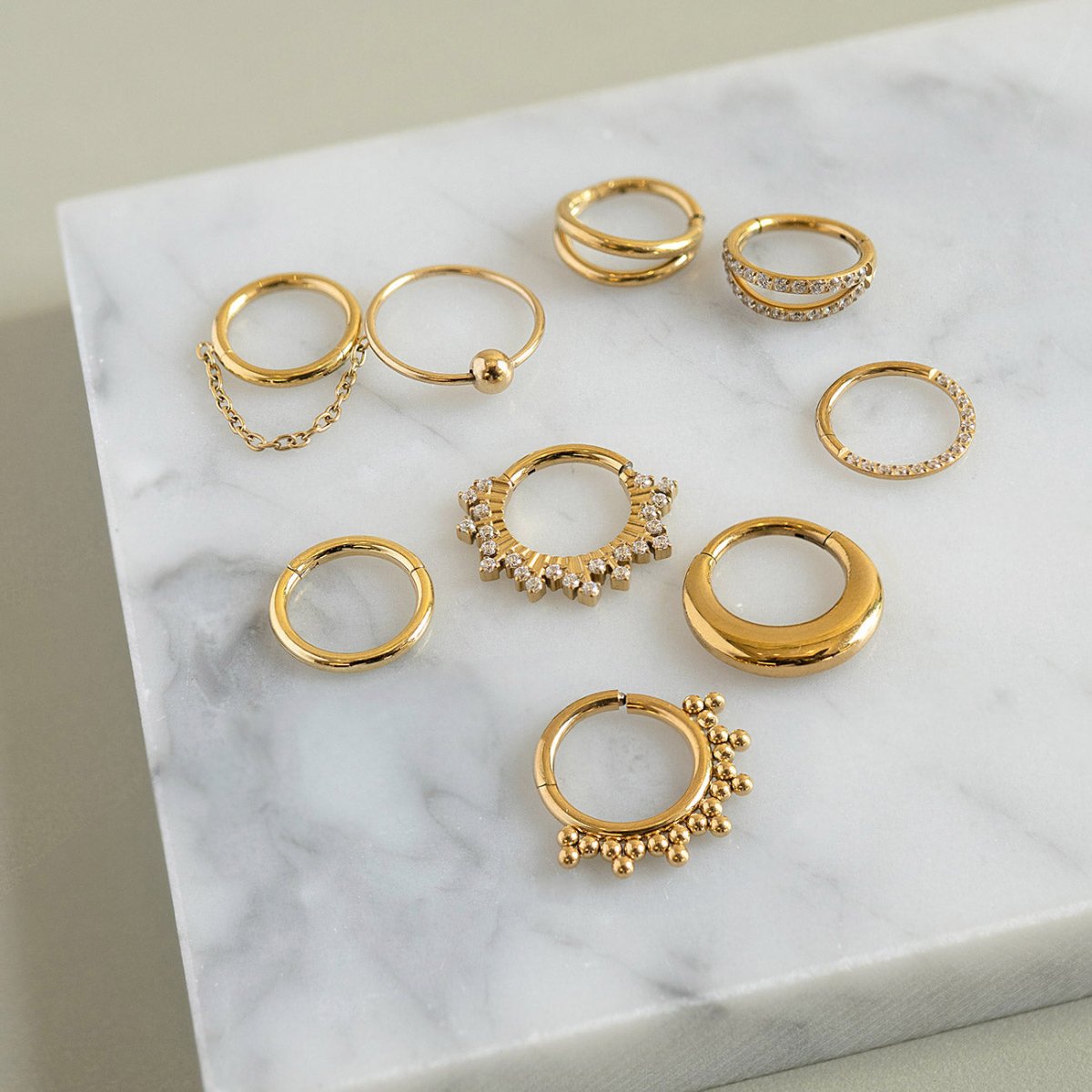 Gold titanium beaded half clicker hoop among assorted clicker hoops on a marble surface