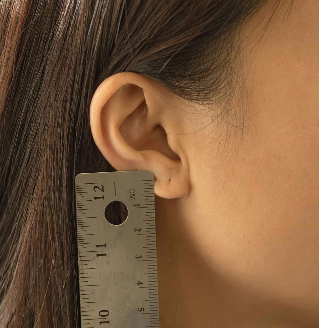Huggie fit guide showing a ruler measuring the height of a model's ear cartilage in centimeters.