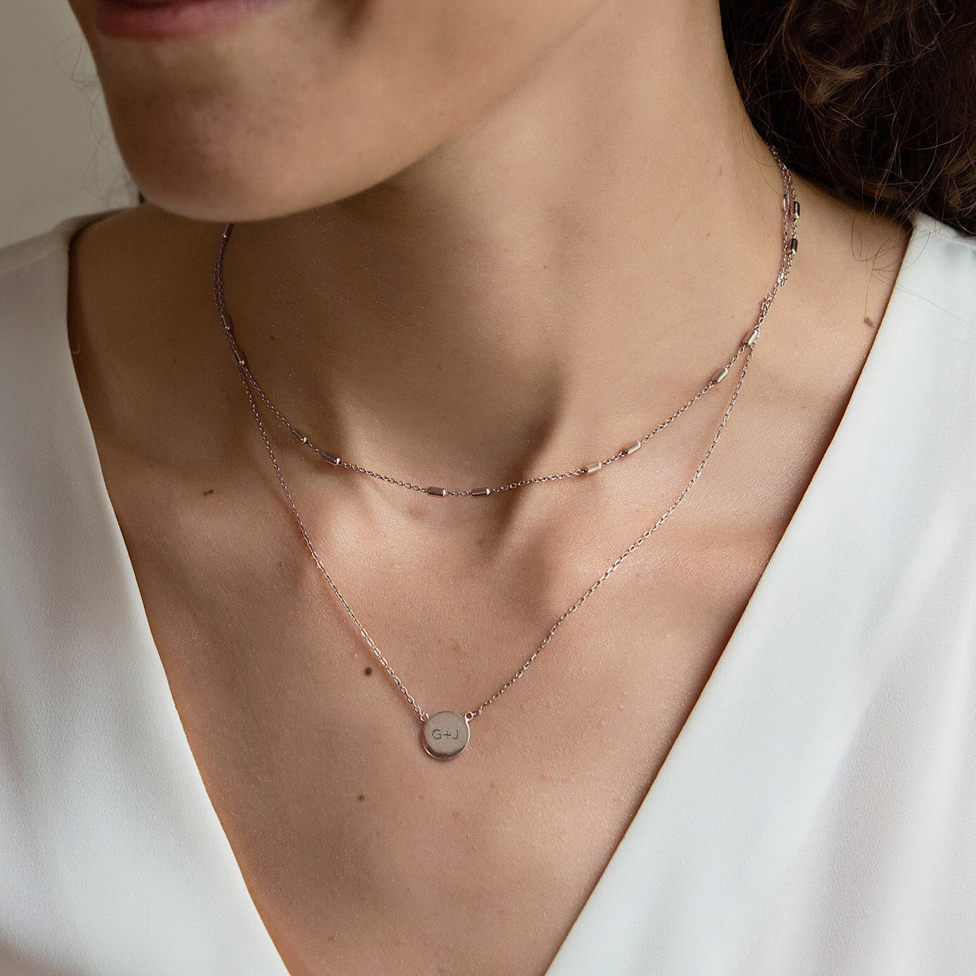 Sterling silver engravable disc necklace engraved with initials, layered on a model's neckline