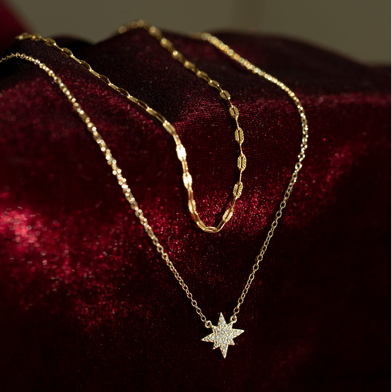 Gold vermeil layered duo of a lace chain and a pavé star pendant chain, on dark red velvet