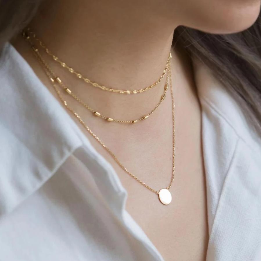 Gold layered necklace set with delicate chains and a small round disc pendant, shown on a model's neckline