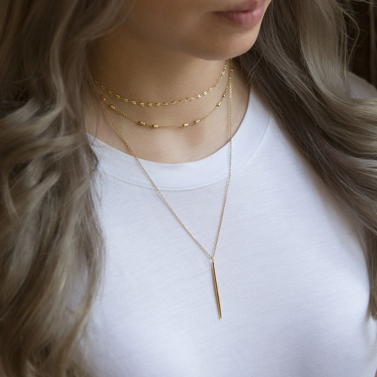 Gold vermeil layered necklace with a long slim needle bar pendant, shown on a model's neckline