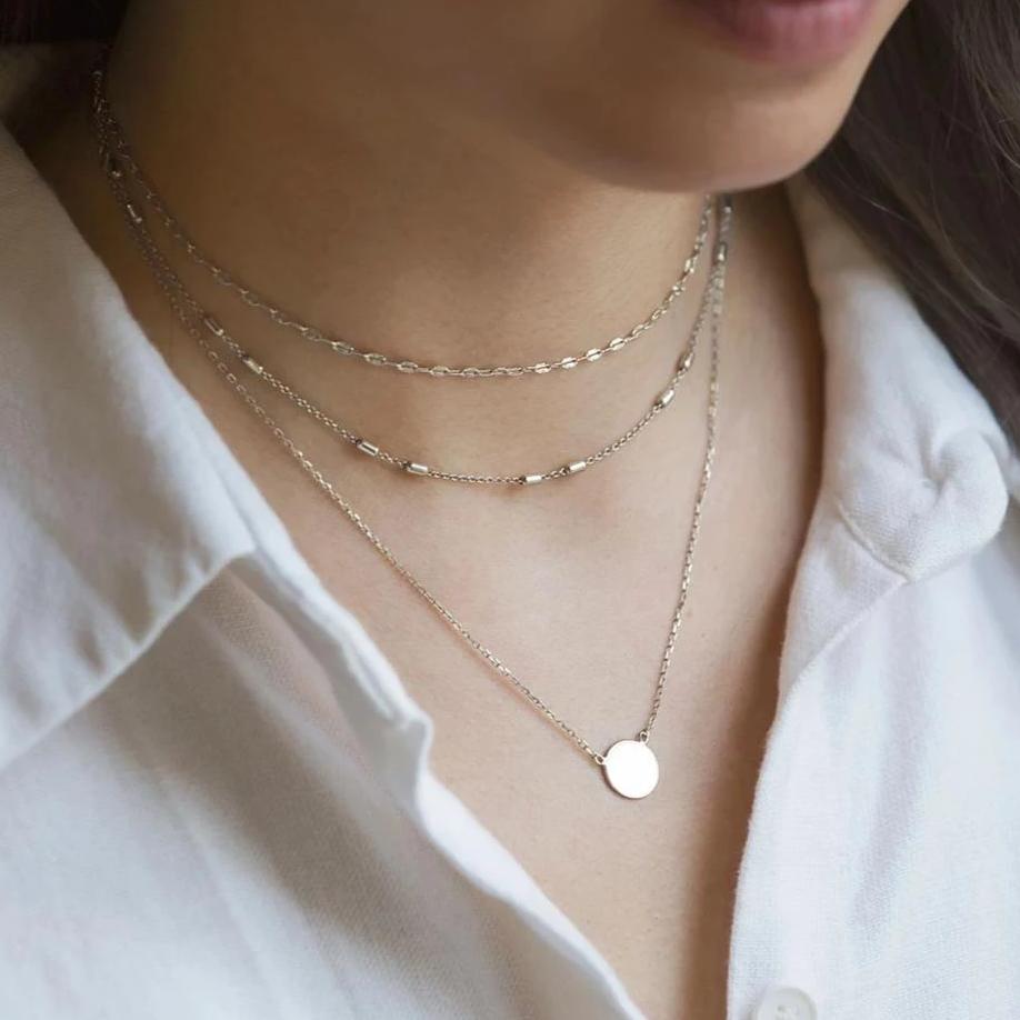 Sterling silver layered necklace set with fine chains and a small round disc pendant, shown on a model's neckline