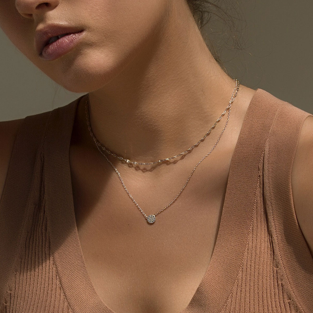 Sterling silver chain choker layered with a round pavé pendant necklace, shown on a model's neckline