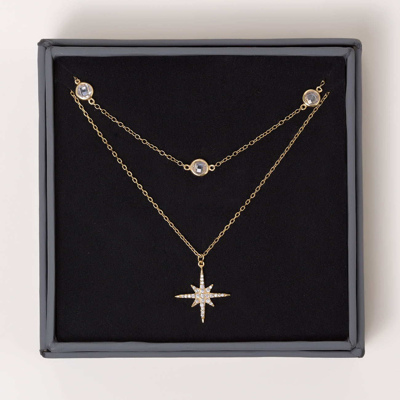 Gold layered necklace with a clear stone station chain and a pavé starburst pendant, in a gift box