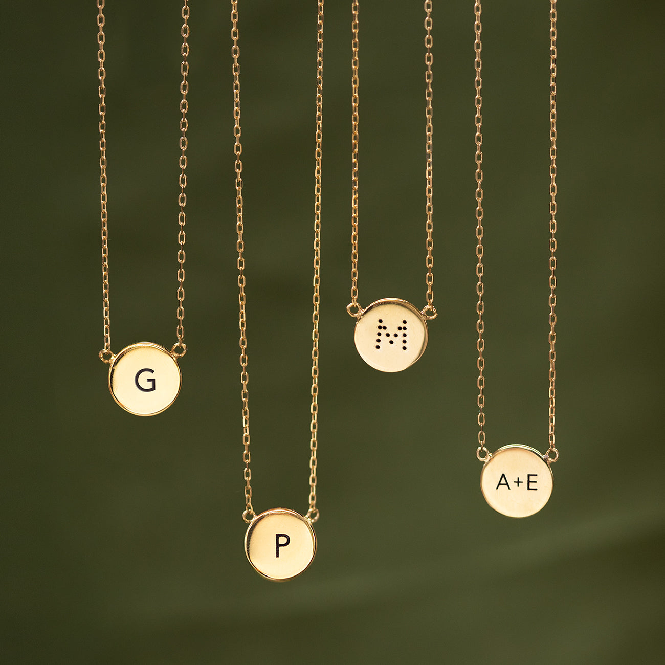 Four gold vermeil engravable disc necklaces engraved with initials, on a green background