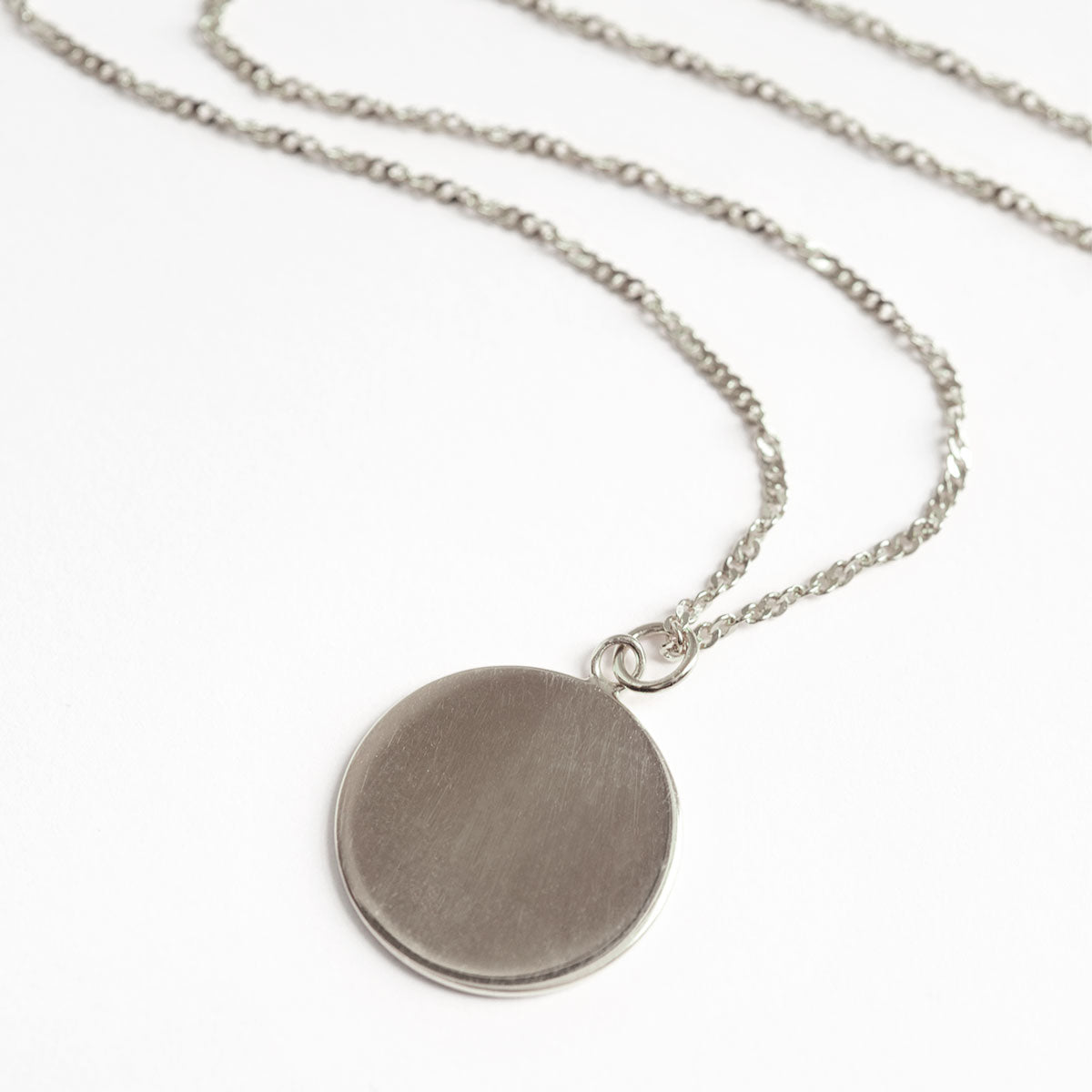 Sterling silver round disc pendant on a twisted chain, laid on a white background