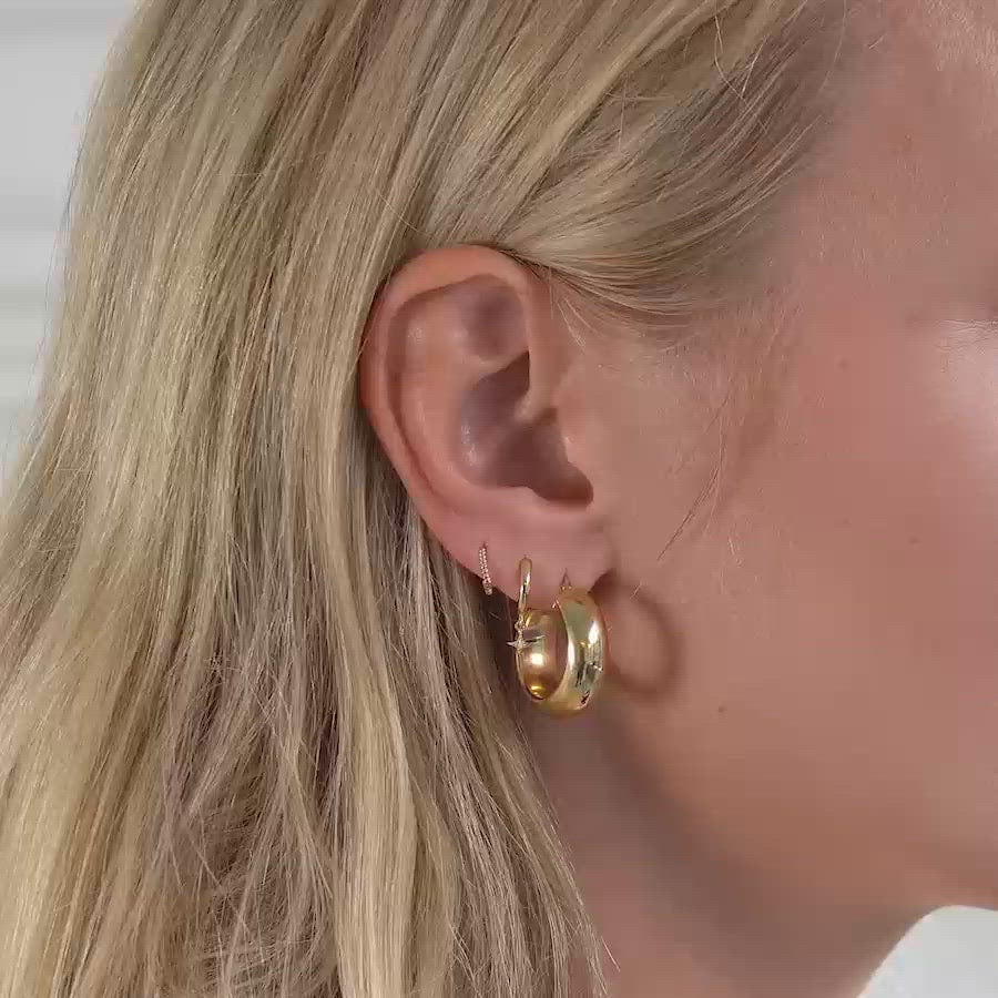 Woman wearing gold chunky hoops, gold star flare huggie earrings, and gold small rope huggie earrings