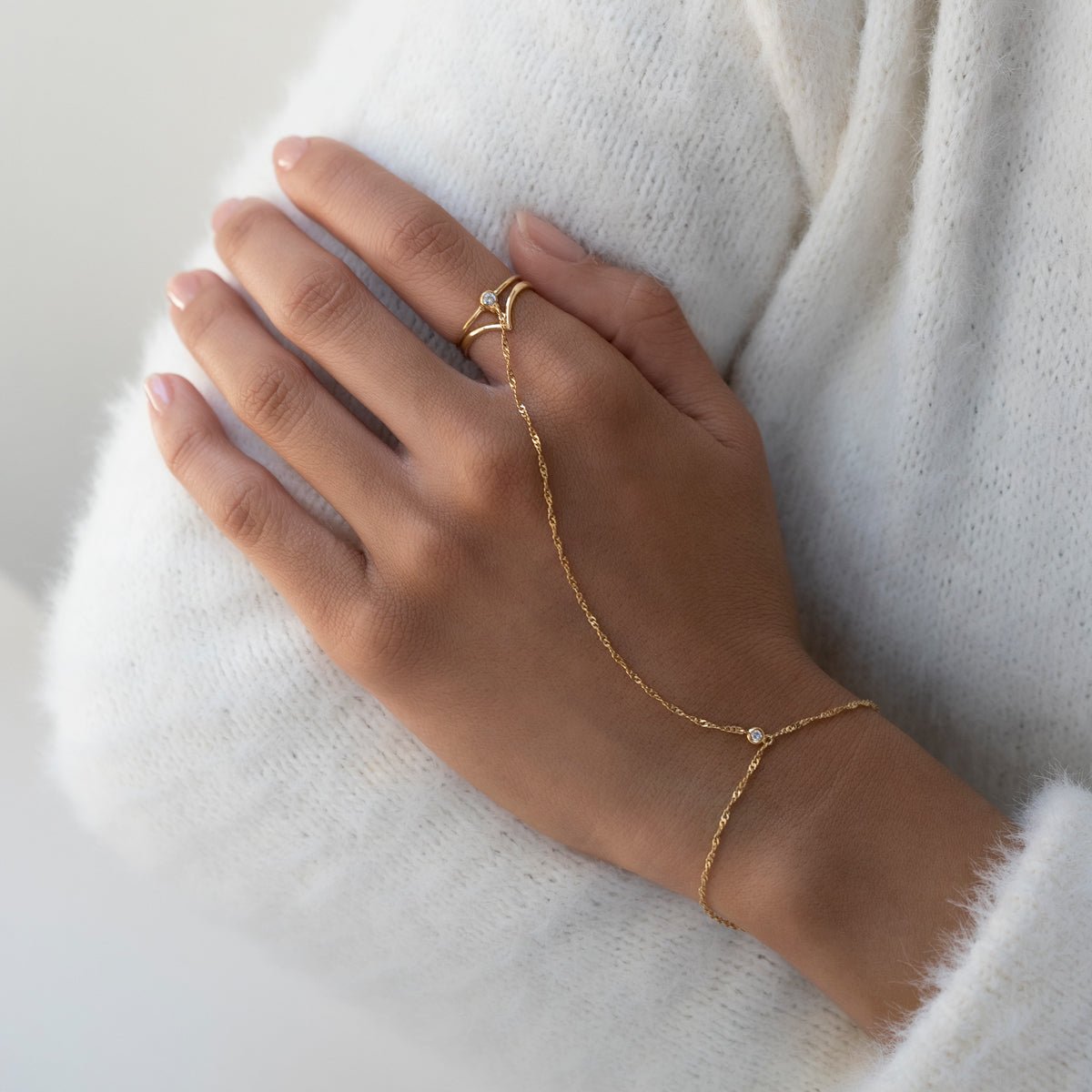 14K gold chevron ring with a clear stone, stacked on a model's finger near a sweater