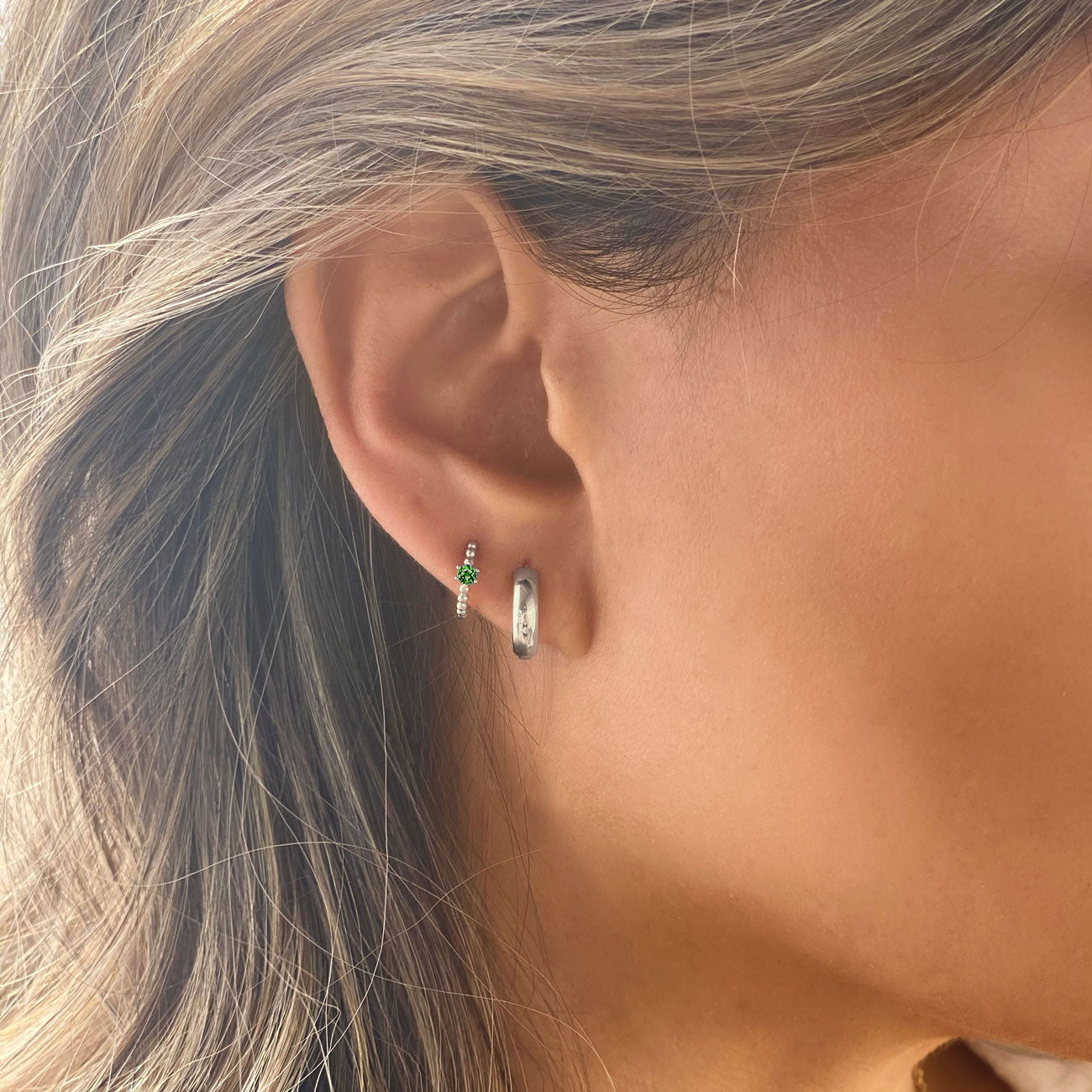 Close-up of woman's ear featuring Sterling Silver Gemstone Bead Huggies Emerald CZ Crystal and Silver Chunky Hoop. 