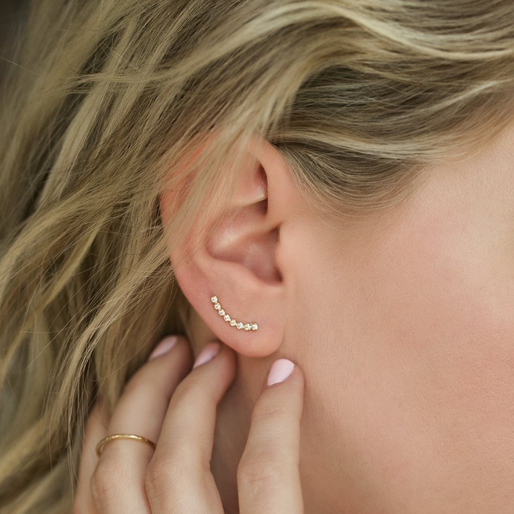 Gold white zirconia ear climber curving up the lobe, shown on a model's ear