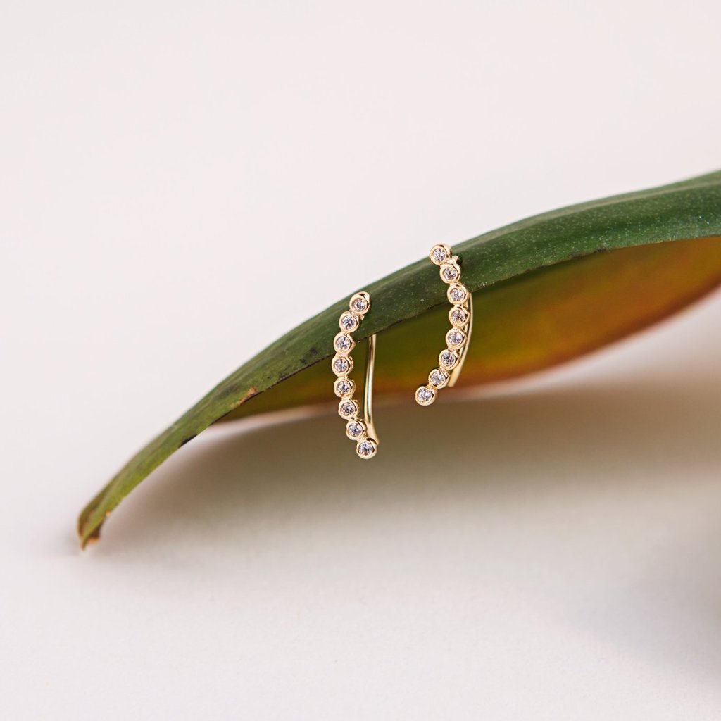 Gold white zirconia ear climbers resting on a green leaf, close-up detail