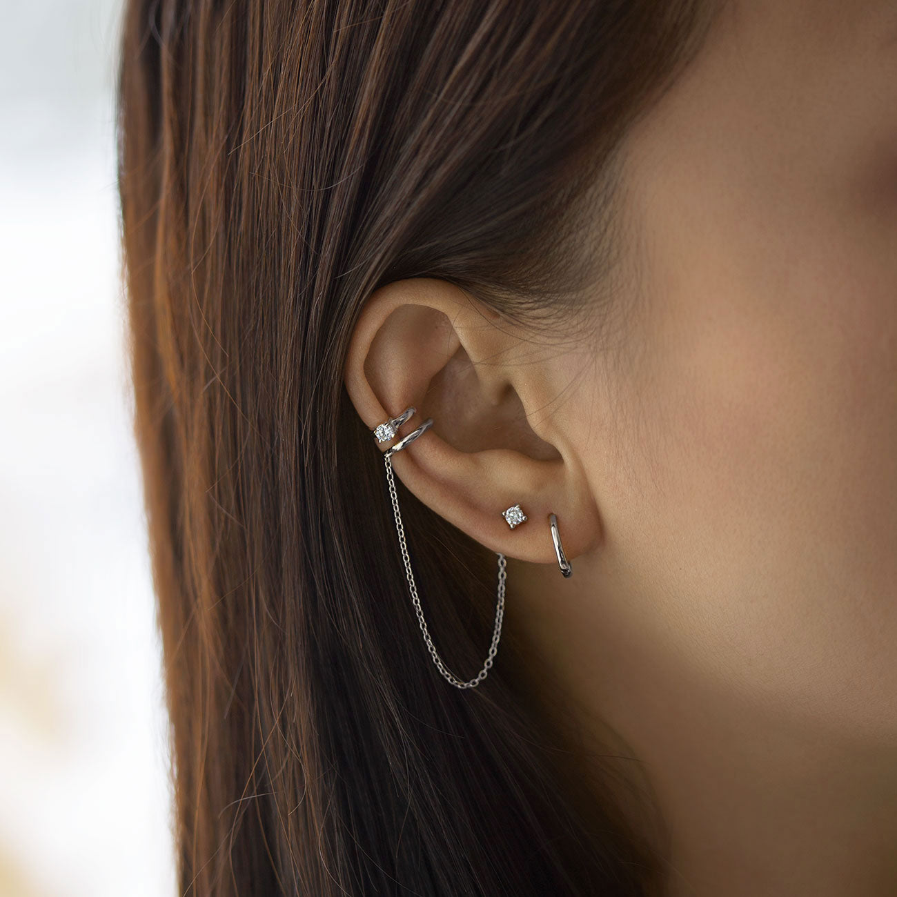 Sterling silver ear cuff with a draped chain and white zirconia stud, shown on a model's ear