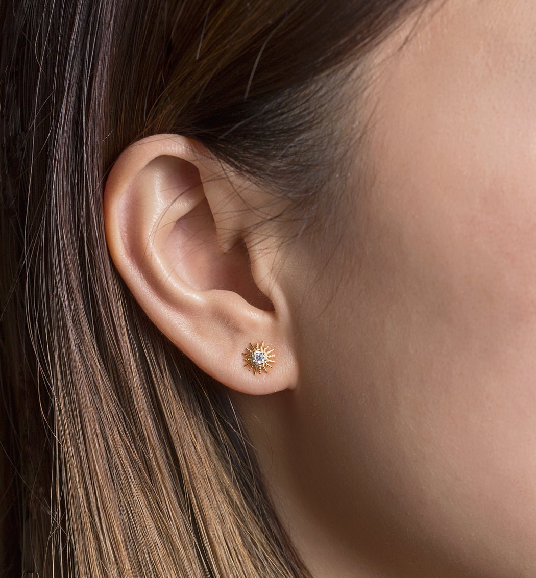 Rose gold vermeil sunburst stud with a clear stone, close-up on a model's lobe against a tan backdrop