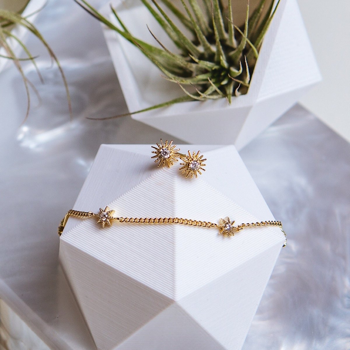 Rose gold vermeil sunburst studs and star station bracelet with clear stones, styled on white blocks