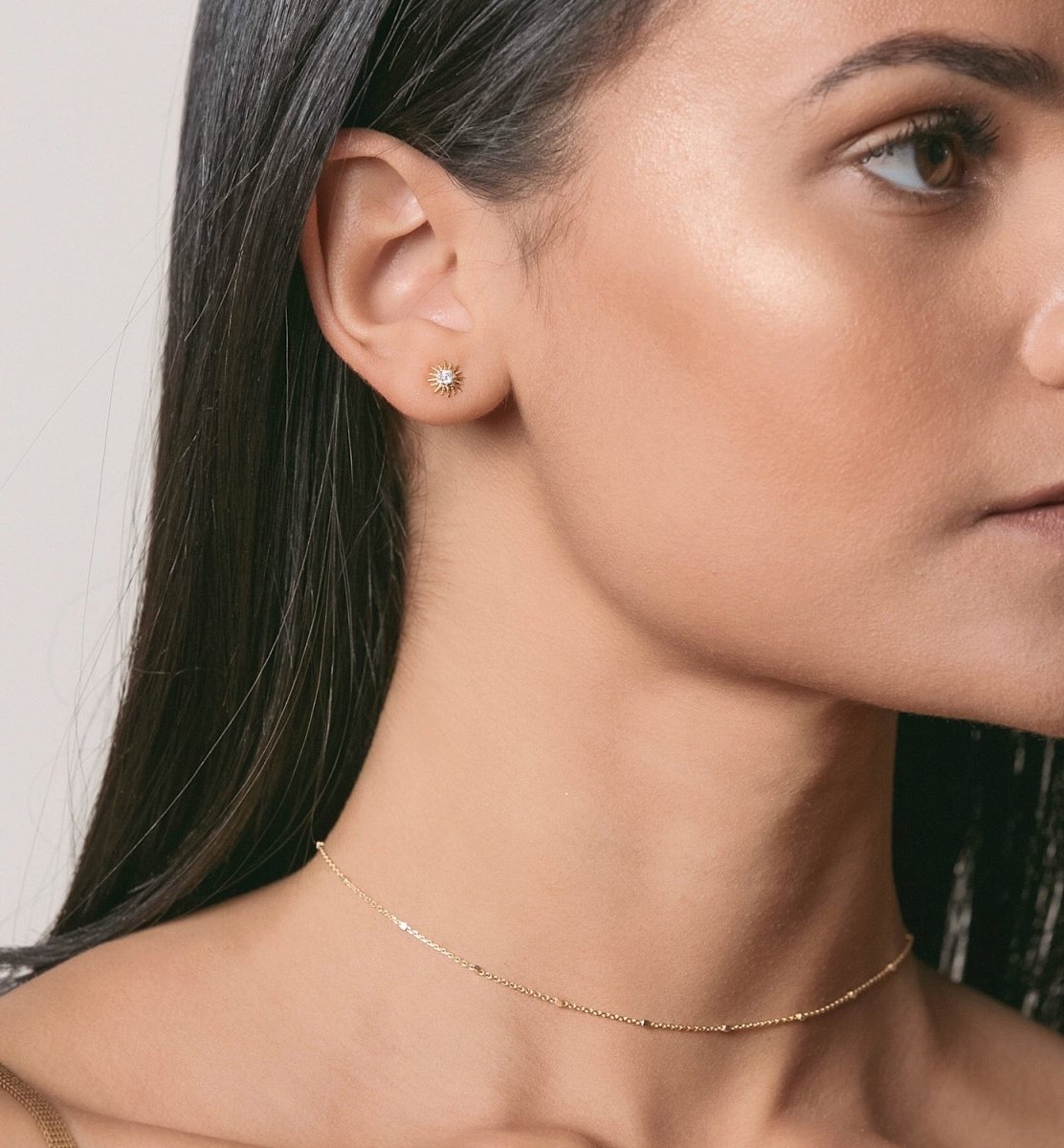 Rose gold vermeil sunburst stud with a clear stone on a model's lobe, with a fine gold chain necklace